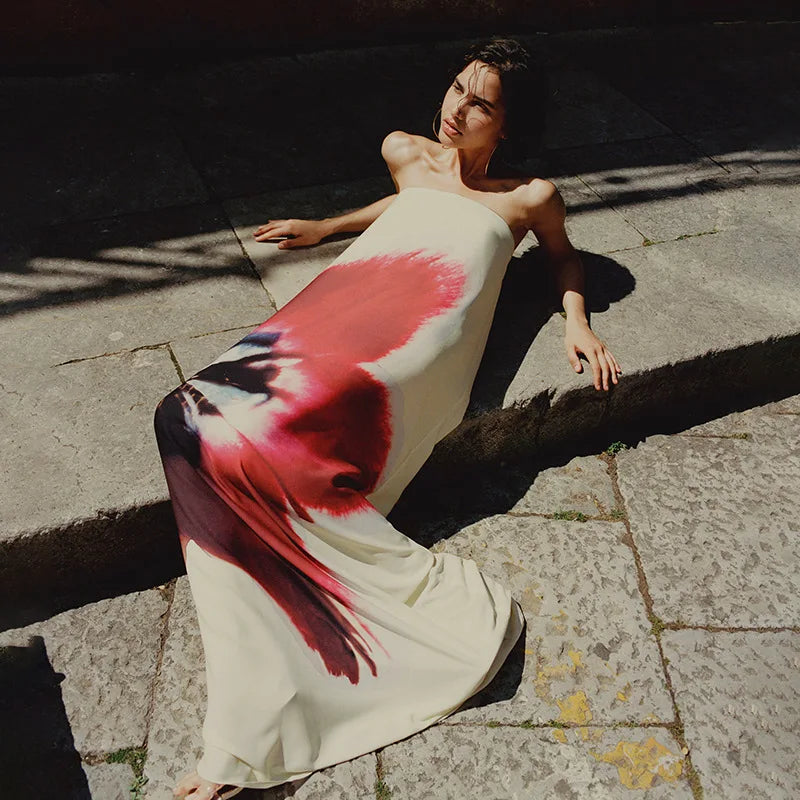 Woman lying on a stone pavement wearing a dress with a red and black abstract design.