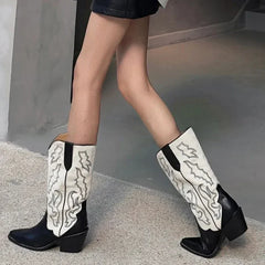 White cowboy boots with black accents worn by a person on a concrete surface.