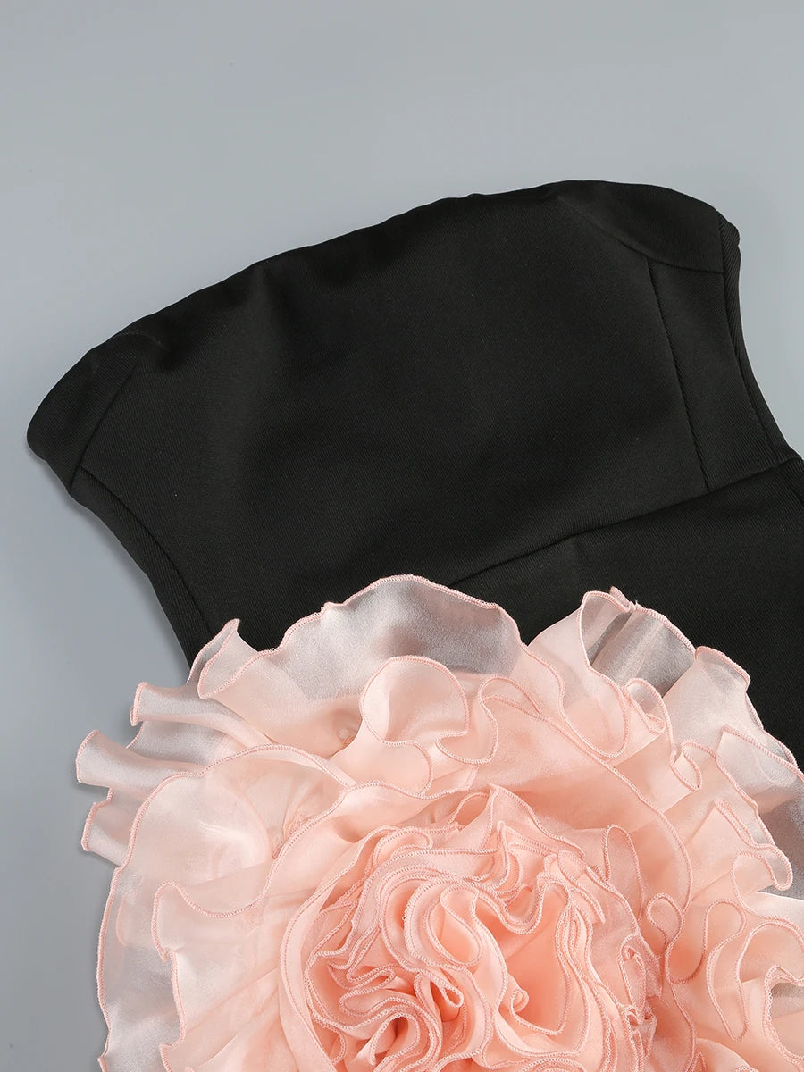 Black dress with a large pink floral embellishment on a gray background