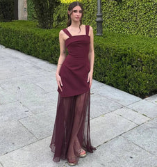 Woman in a burgundy dress standing on a sidewalk with greenery in the background