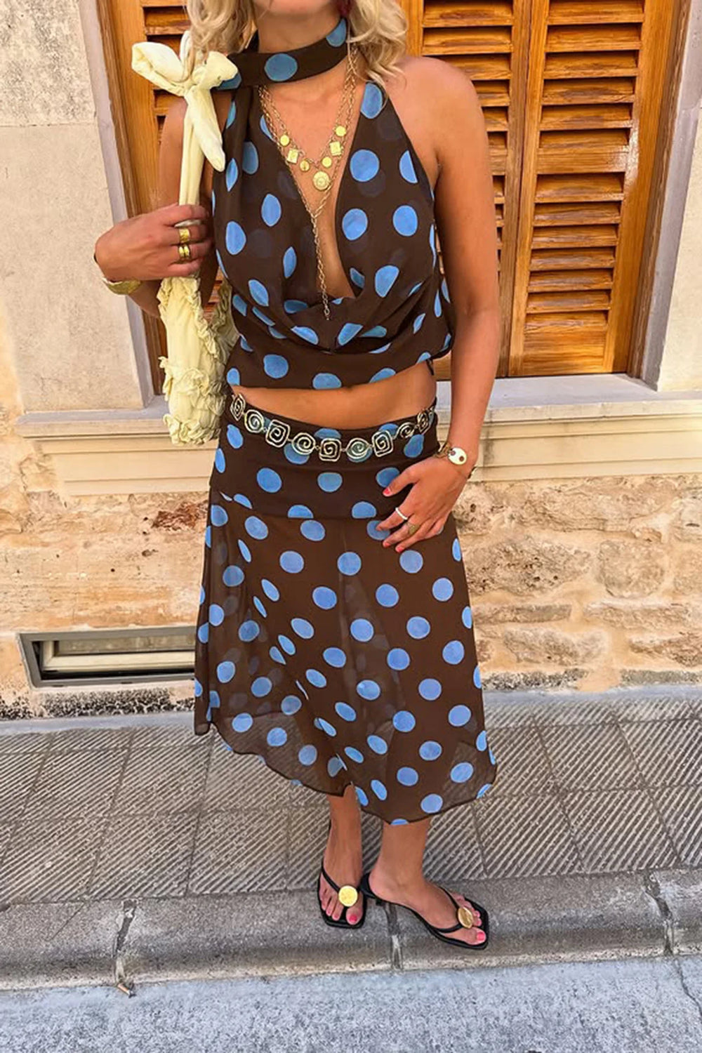 Woman wearing a brown dress with blue polka dots, standing on a street.