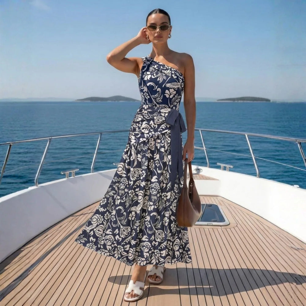 Woman wearing navy and white print one-shoulder swimwear with a flowing skirt on a yacht deck.