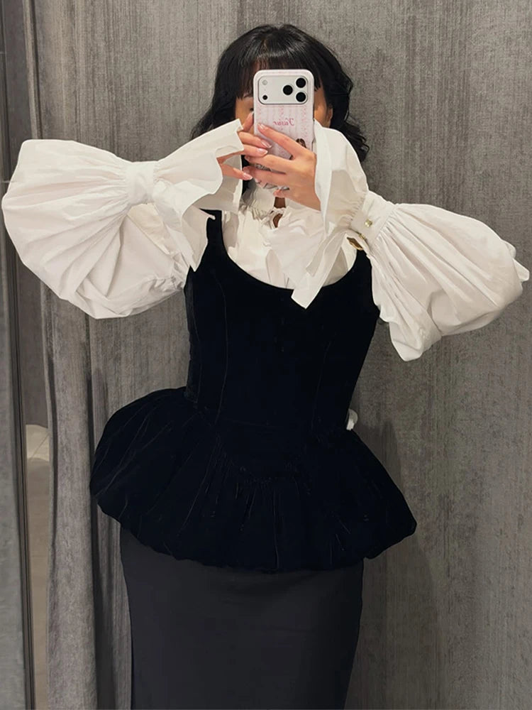 Person wearing a black dress with a white blouse featuring large sleeves against a gray curtain background.