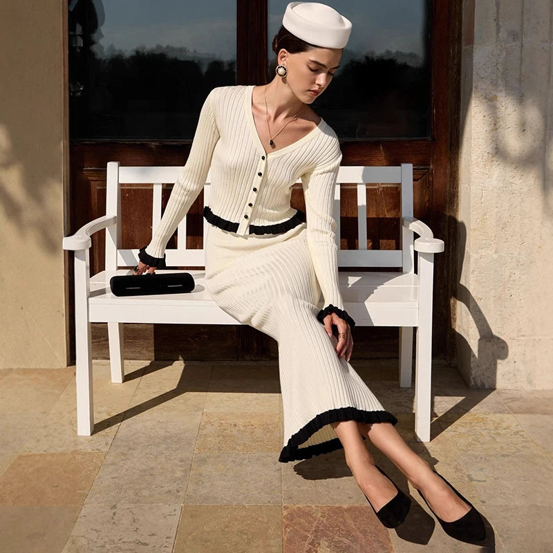 Woman in a white outfit with black details sitting on a white bench outdoors.