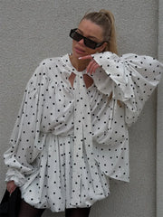 Woman wearing a white polka dot dress against a gray wall