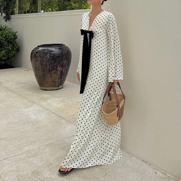 Woman in a long polka dot dress holding a woven bag outdoors.