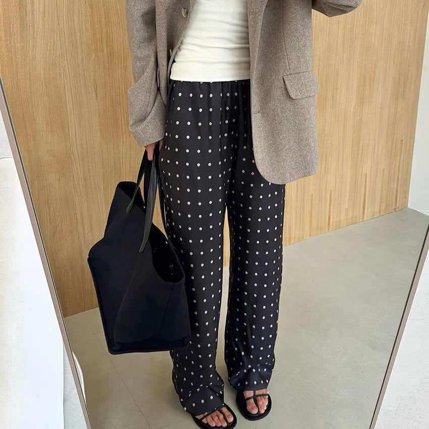 Person wearing polka dot pants and a gray blazer holding a black bag indoors.