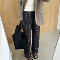 Person wearing polka dot pants and a gray blazer holding a black bag indoors.