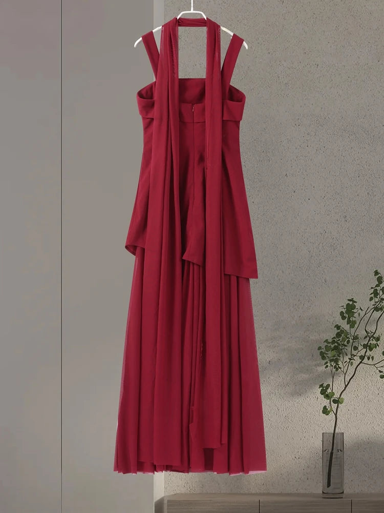 Red dress on a hanger against a neutral wall with a plant in the corner.