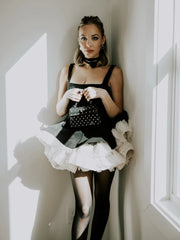 A woman in a black and white dress holding a black studded handbag against a white wall.