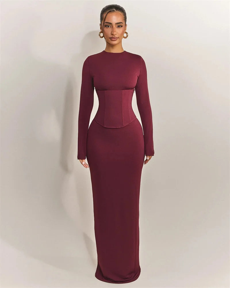 Woman wearing a burgundy long-sleeve gown against a plain background