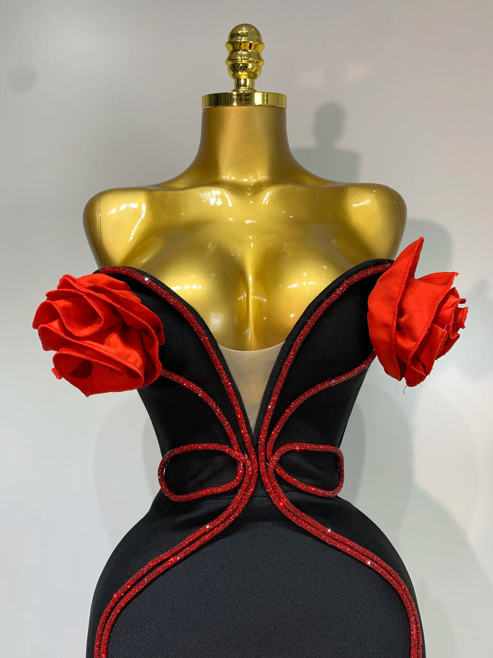 Black evening gown with red floral accents on a gold mannequin against a white background