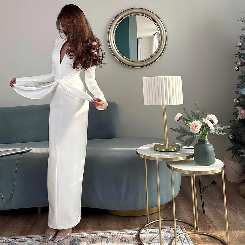 Woman in a white dress standing in a modern living room with a Christmas tree.