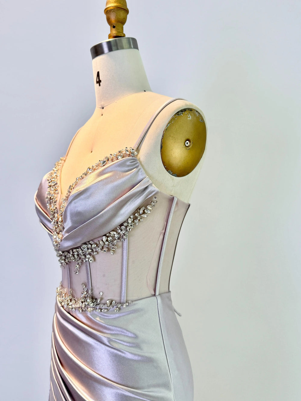 Silver evening gown with bead detailing on a mannequin against a light gray background