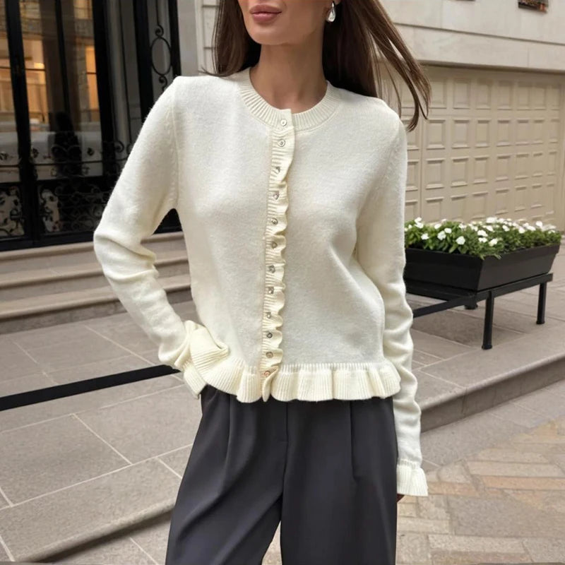 Woman wearing frill trim knit cardigan with pleated skirt outside a townhouse entrance