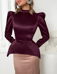 Woman wearing a burgundy satin top with puffed sleeves against a white wall.
