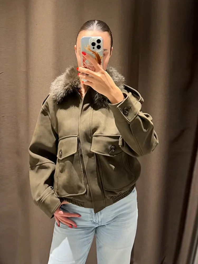 Person wearing a green jacket with fur collar taking a mirror selfie against a brown curtain.