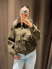 Person wearing a green jacket with fur collar taking a mirror selfie against a brown curtain.