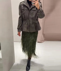 Person wearing a plaid jacket and green skirt with black boots in a neutral setting.