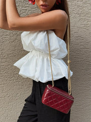 Woman holding a red quilted handbag against a beige wall