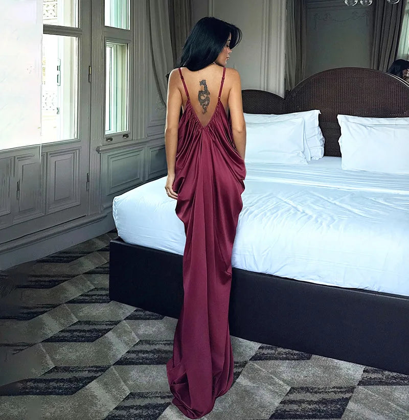 Woman in a burgundy evening gown standing by a bed in a bedroom.