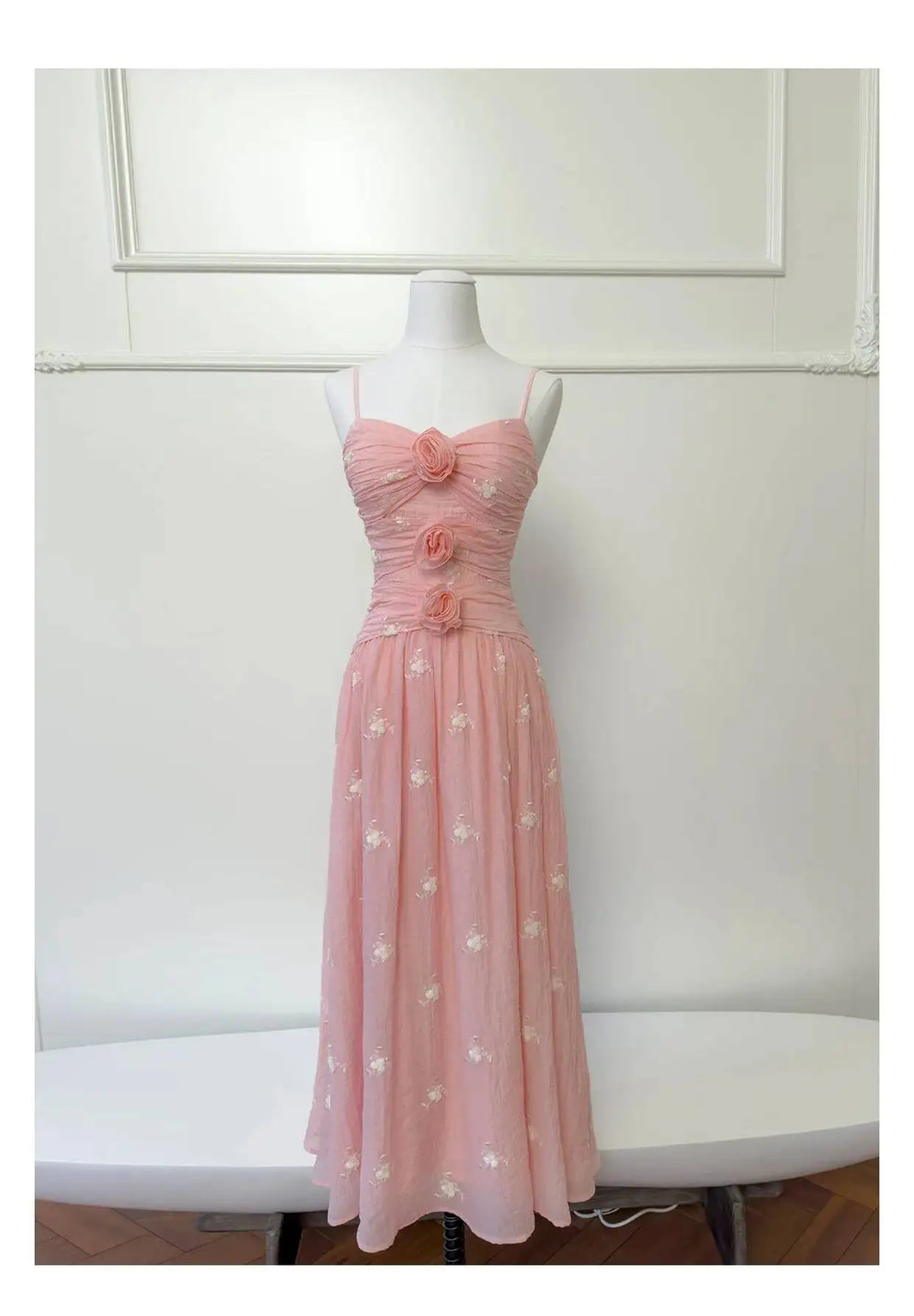 Pink embroidered midi dress with rose embellishments displayed on a white surface