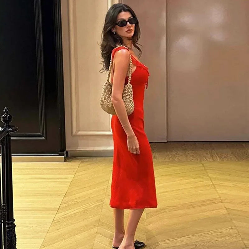 Woman in a red dress and sunglasses holding a beige handbag indoors.