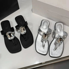 Square toe flat sandals with a prominent crystal embellishment on the strap.