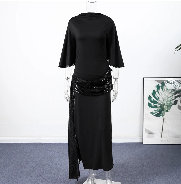 Mannequin wearing a black outfit with sequin details in a room with a plant and framed picture on the wall.