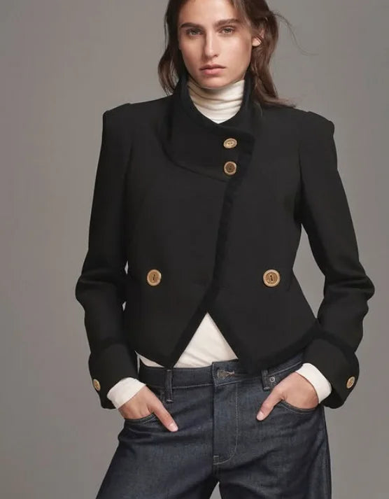 Woman wearing a black jacket with gold buttons on a gray background