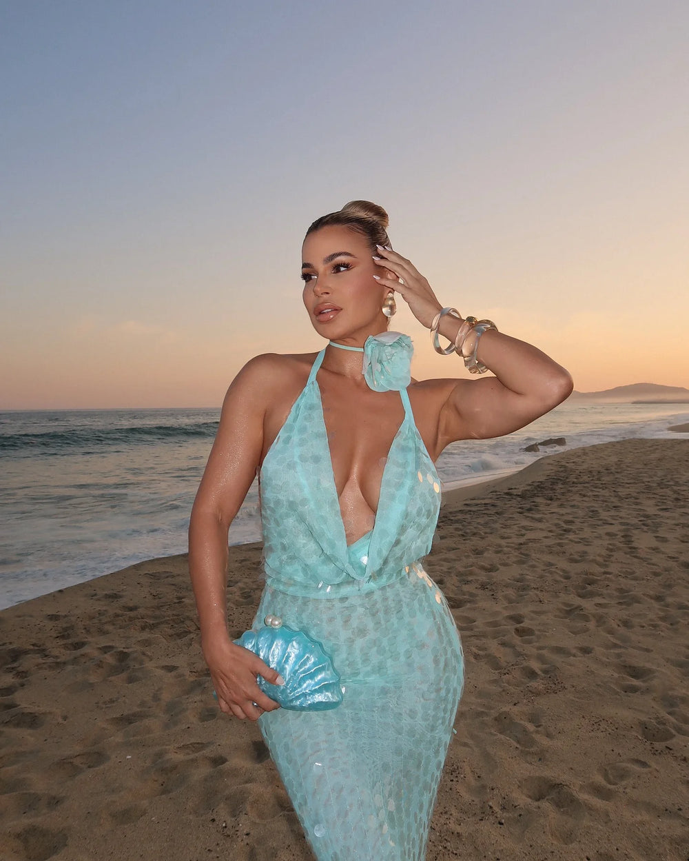 Woman in a light blue dress standing on a beach at sunset