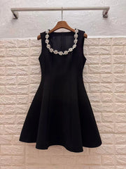 Black dress with floral embellishments on a hanger against a textured wall.