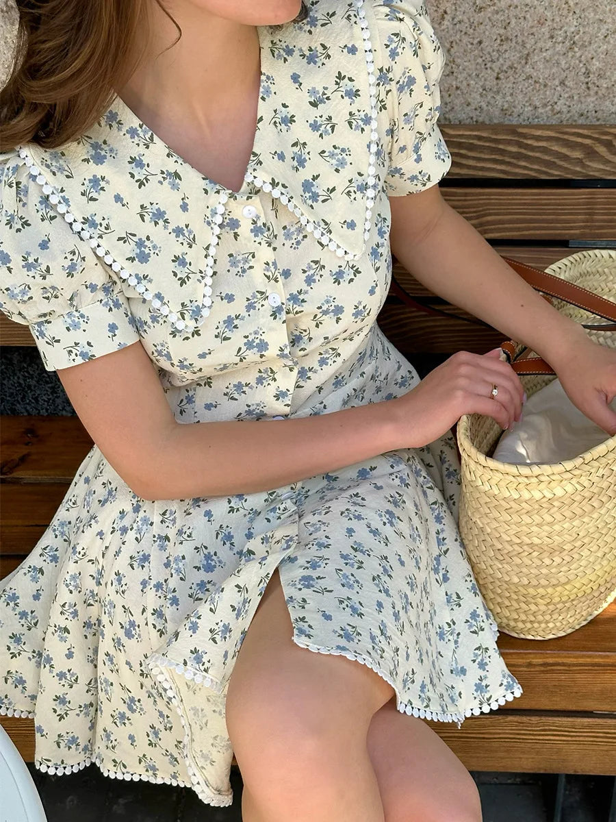 Woman in a floral dress sitting on a wooden bench with a straw bag.