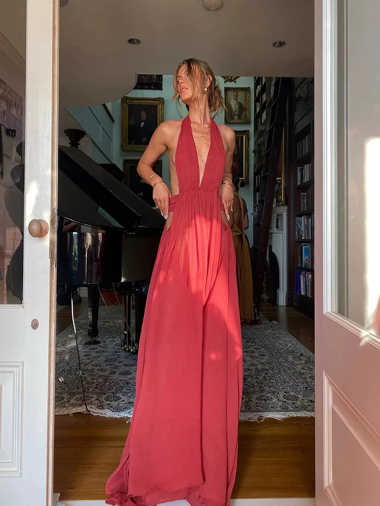 Woman in a long red dress standing in a room with a piano and bookshelf.