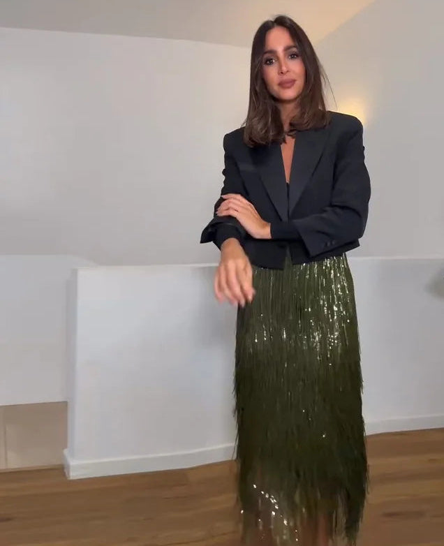 Woman wearing a black blazer and green sequin skirt in a room.