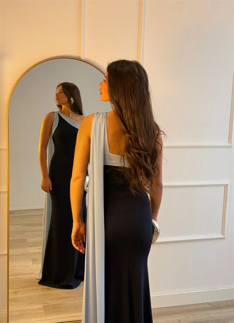 Woman in a long black dress standing in front of a mirror.