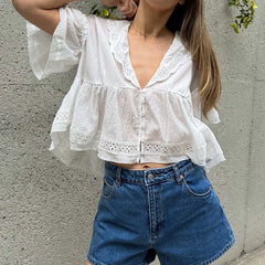 Person wearing a white blouse with ruffled sleeves and blue jeans against a gray wall.