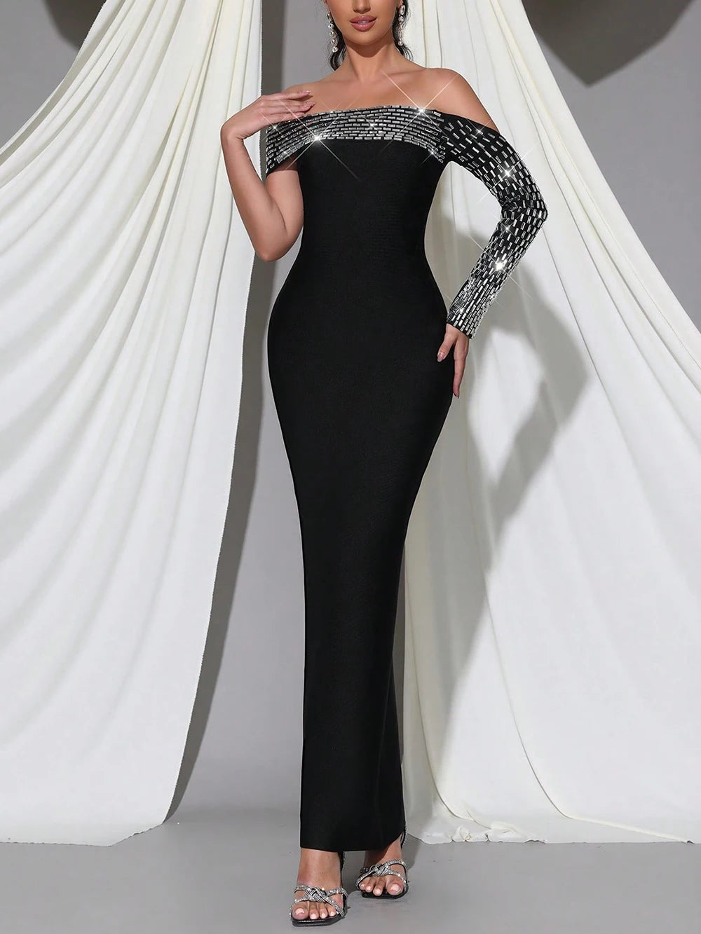 Black off-shoulder evening gown with sequin details on a white draped background