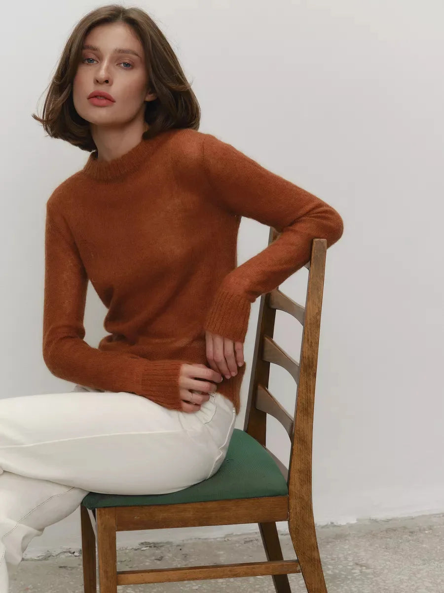 Woman wearing a brown sweater and white pants sitting on a wooden chair with a green cushion.