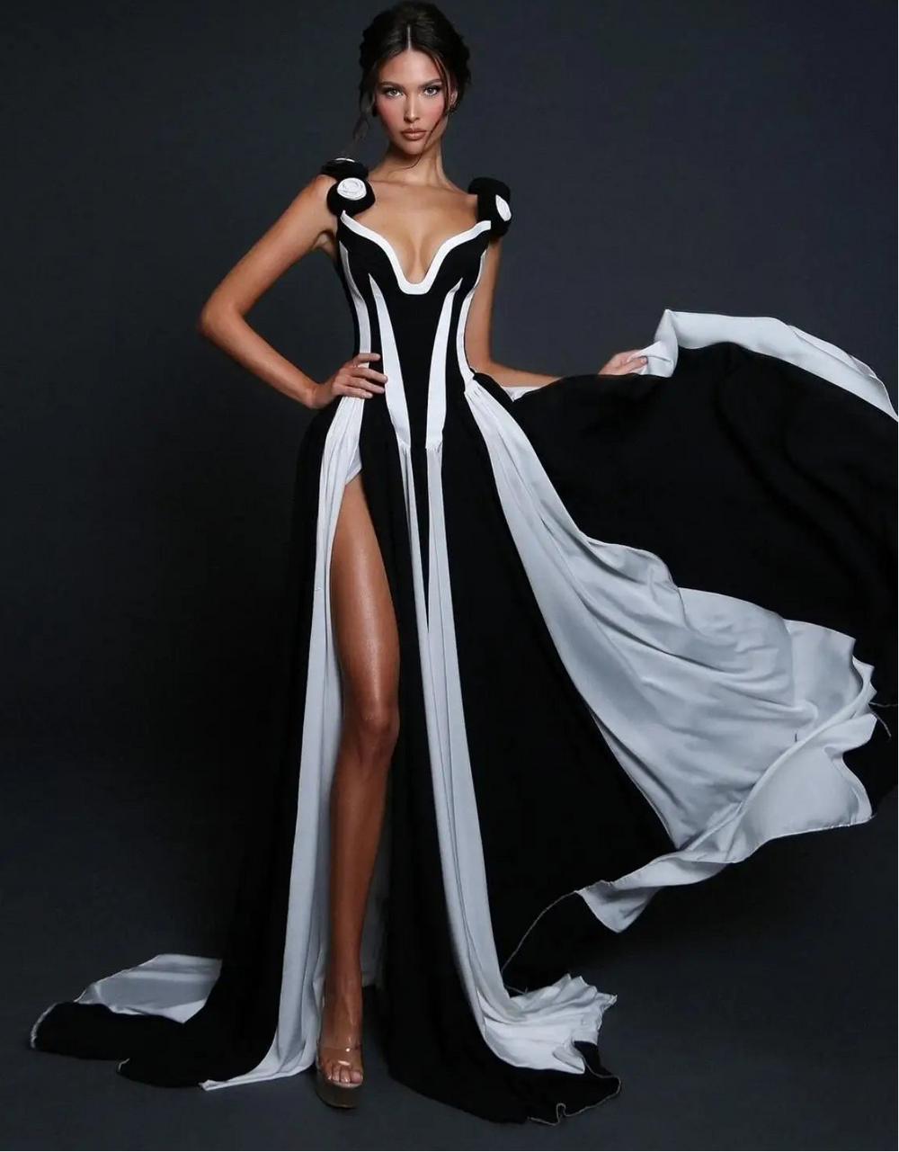 Model wearing a black and white dress with a long train on a dark background