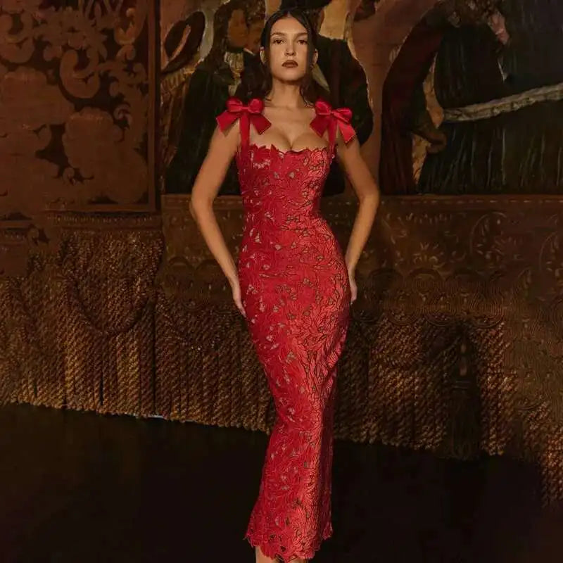 Woman in a red dress with bow details standing against an ornate wall.
