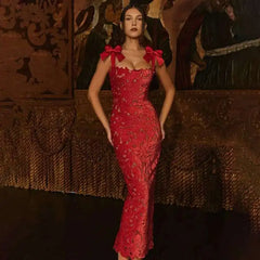 Woman in a red dress with bow details standing against an ornate wall.