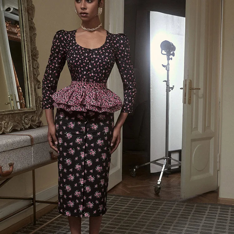 Woman wearing a floral dress with a peplum top in a room with a mirror and camera equipment.