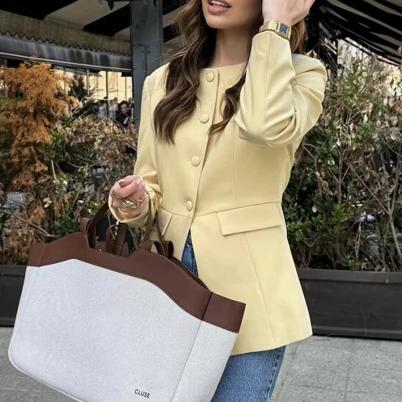 Woman in a yellow coat holding a white and brown handbag outdoors.