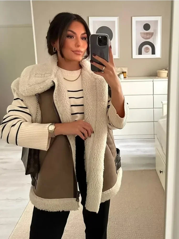 Woman taking a mirror selfie wearing a brown coat with white fur trim in a room.
