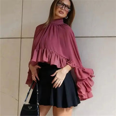Woman wearing a pink blouse with ruffled layers and a black skirt against a neutral wall.