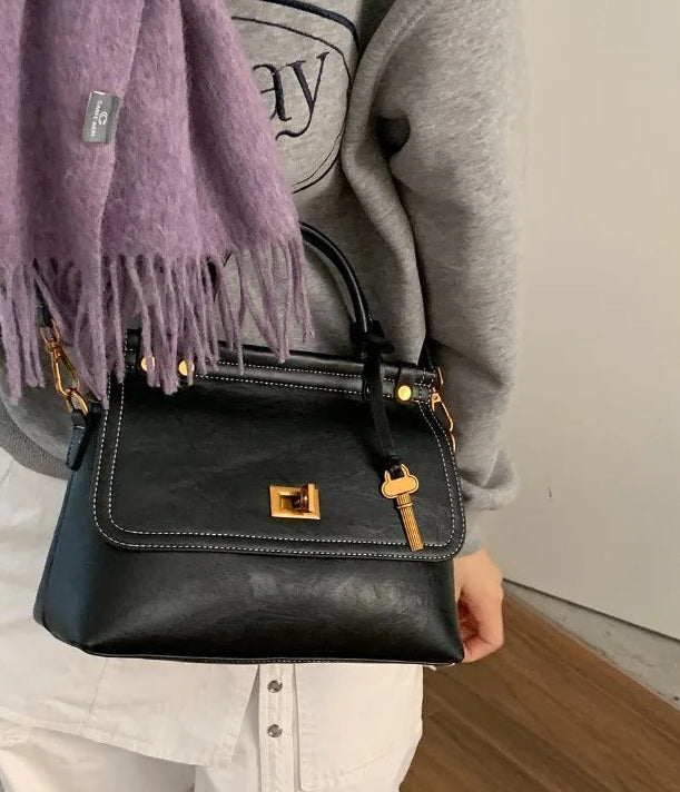 Black handbag with gold accents held by a person wearing a gray sweater and purple scarf.