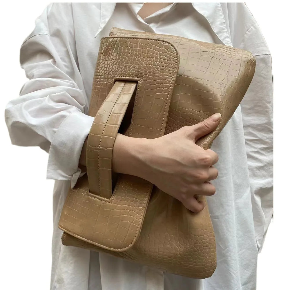Beige crocodile-textured clutch bag held by a person wearing a white shirt.