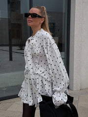 Woman wearing a white blouse with black polka dots and sunglasses outdoors.