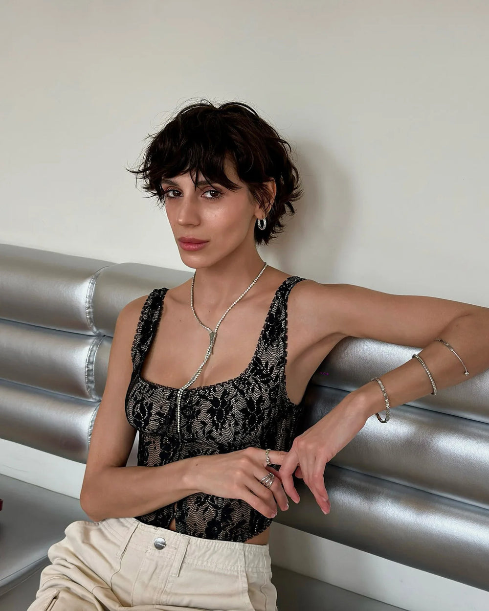Woman posing on a metallic surface wearing a black lace top and beige pants.